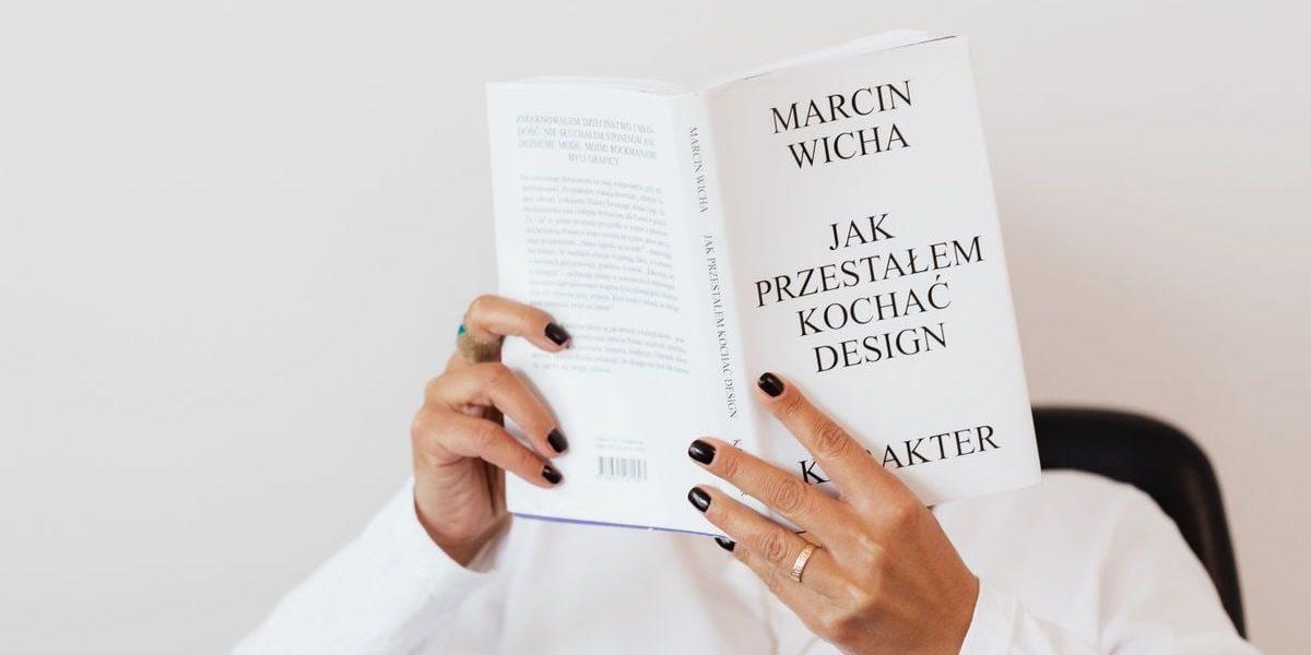 Anonymous female in white shirt with gold chain on neck reading interesting book covering face while sitting on black chair