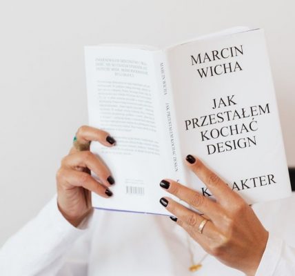 Anonymous female in white shirt with gold chain on neck reading interesting book covering face while sitting on black chair