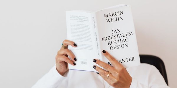 Anonymous female in white shirt with gold chain on neck reading interesting book covering face while sitting on black chair