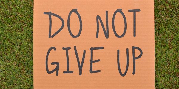 Cardboard sign reading 'Do Not Give Up' placed on green turf, symbolizing perseverance.